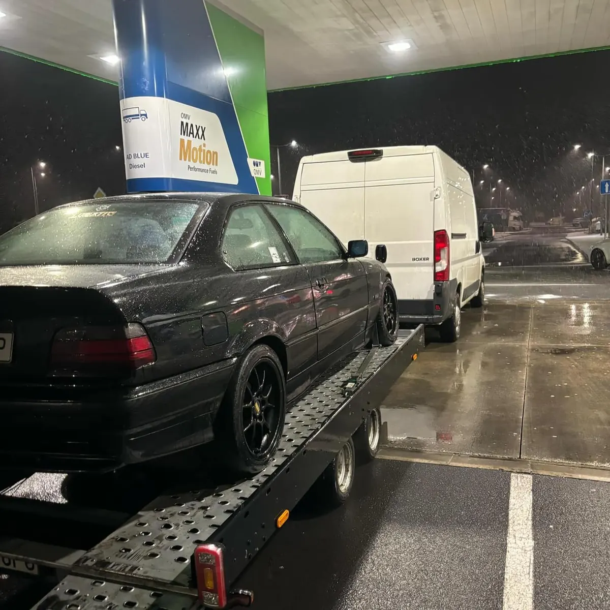 E36 na autoprívese za dodávkou, noc na čerpacej stanici